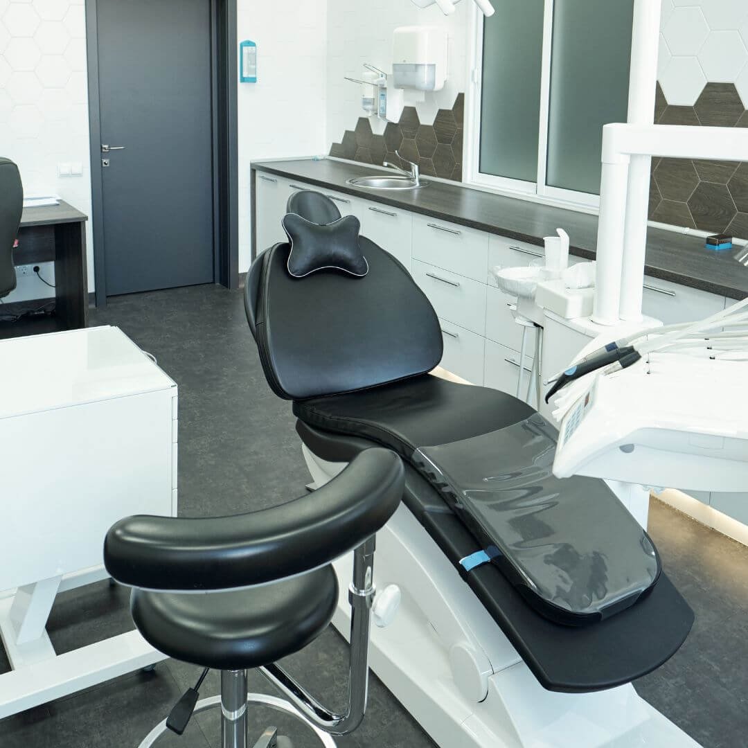 A clean black dental chair in a modern office with dark grey flooring and white cabinetry.