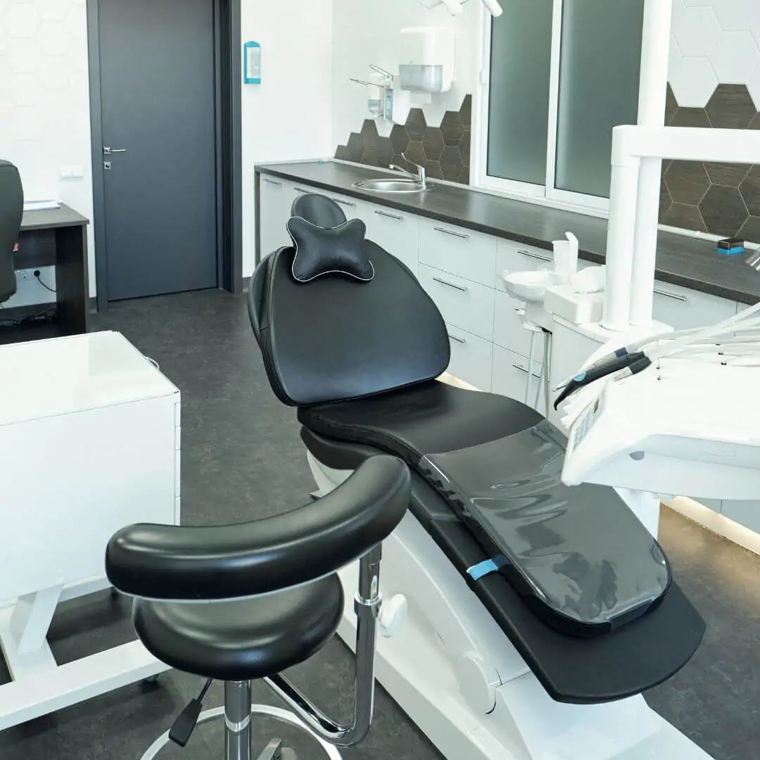 A clean black dental chair in a modern office with dark grey flooring and white cabinetry.